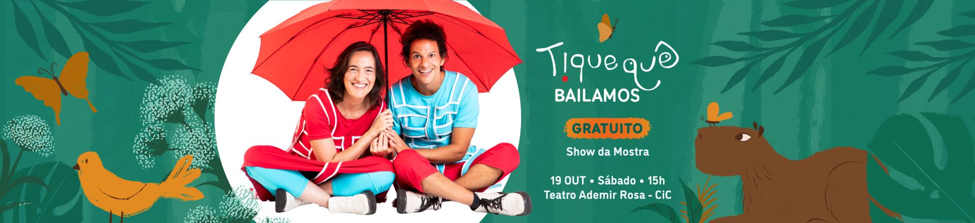 O banner promocional de um evento infantil mostra duas pessoas sorridentes sentadas no chão, sob um guarda-chuva vermelho aberto. A pessoa à esquerda veste uma camiseta vermelha e calça azul, enquanto a pessoa à direita usa uma camiseta azul e calça vermelha. O fundo é verde, com ilustrações de folhas, uma capivara, uma borboleta laranja e um pássaro amarelo. O texto à direita informa: 